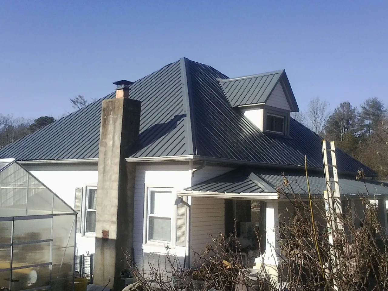 Dark blue standing seam metal roof on a white farmhouse with dormer — Slate & Tile Roof Repair by Roofing Brothers in Point Lookout