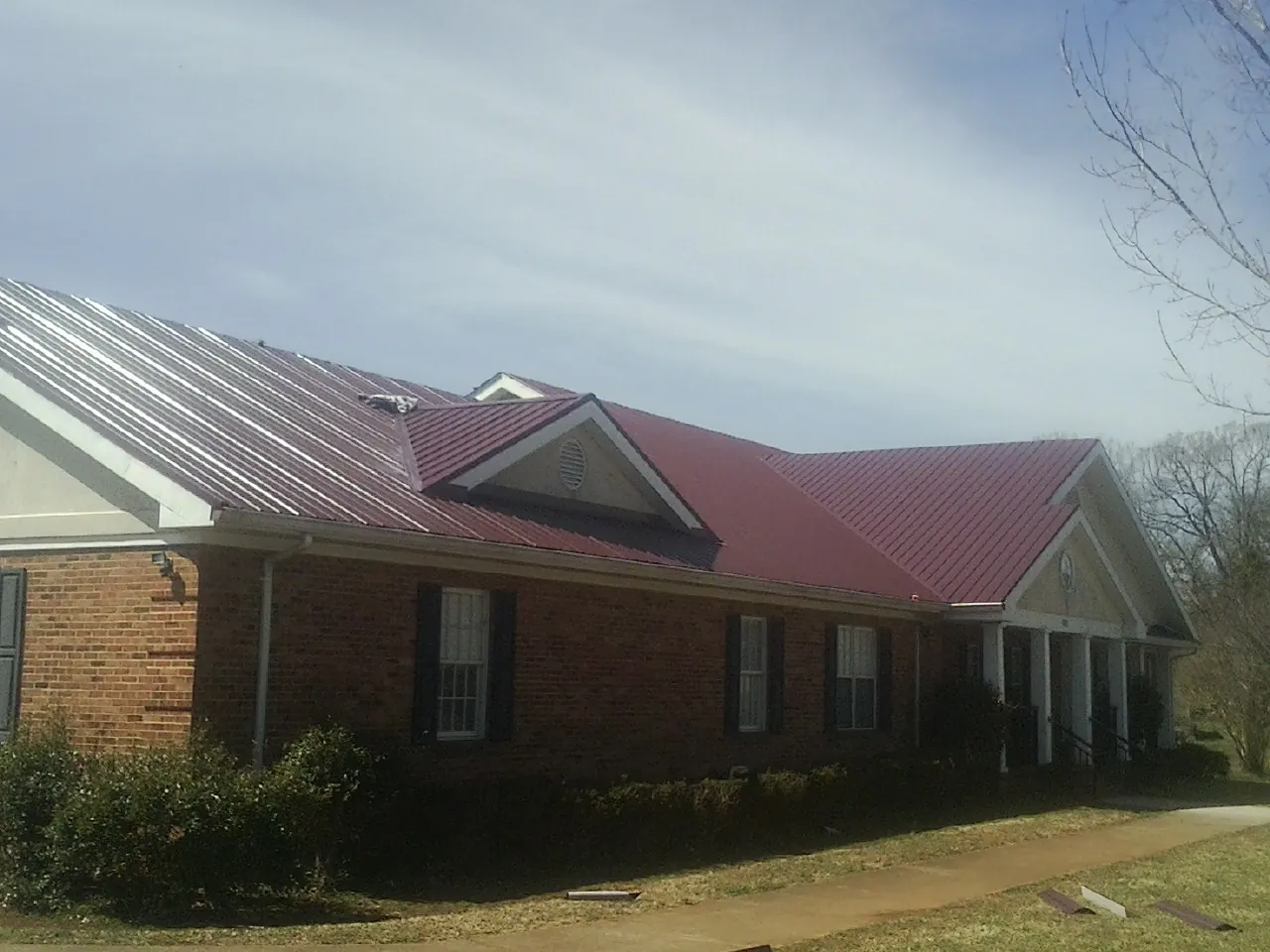 Red metal roof with gabled entries on a long brick building, from a Hail Damage Roof Repair job in Point Lookout