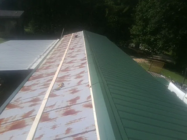 Old rusted panels beside newly installed green metal roofing — Wind Damage Roof Repair by Roofing Brothers in Point Lookout