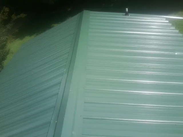 New green metal panels meeting at the ridge of a roof — Flat Roof Repair work by our crew in Point Lookout