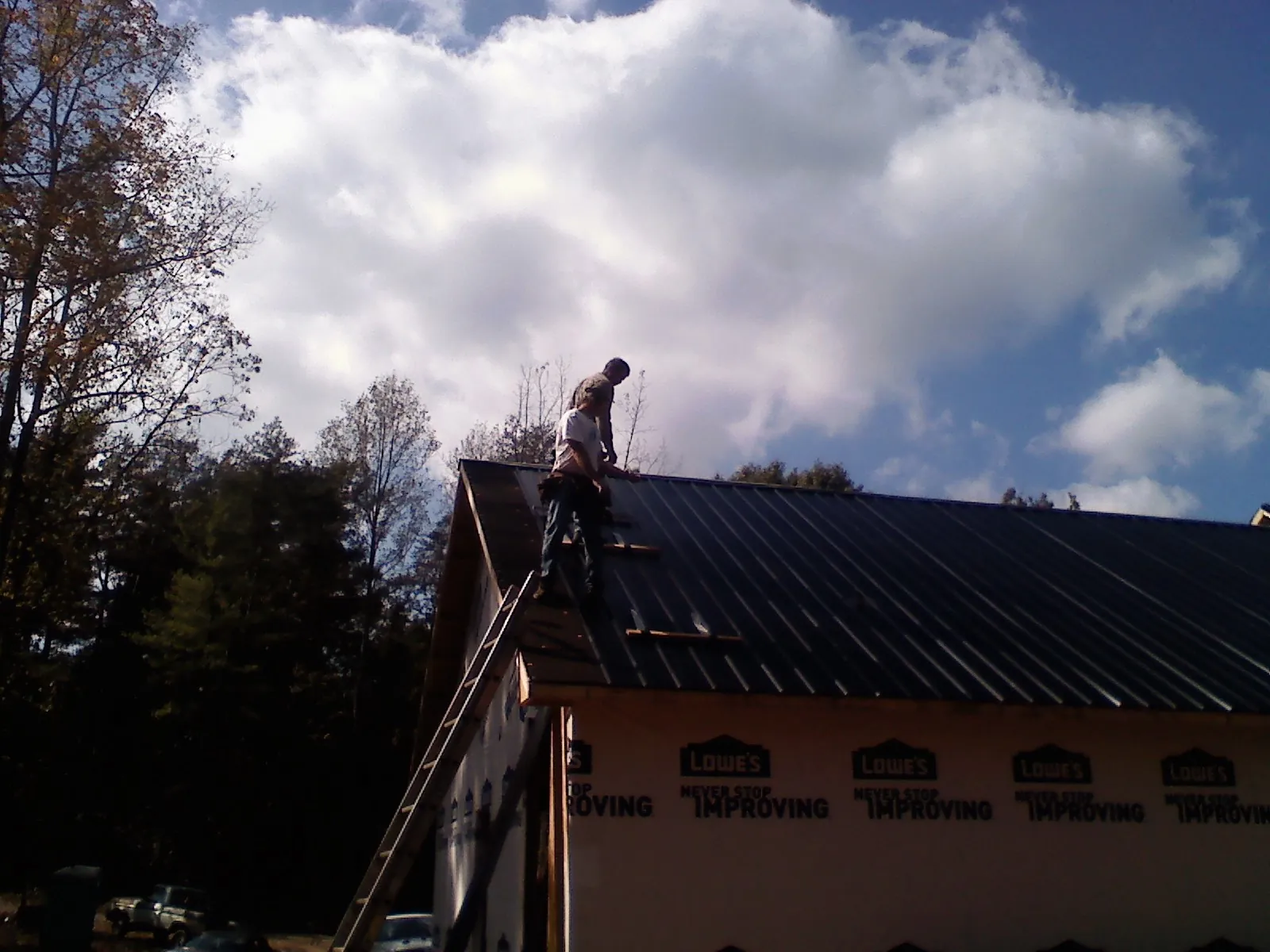 Roofer fastening dark metal panels high against a cloudy sky, from a Roof Inspection job in Point Lookout