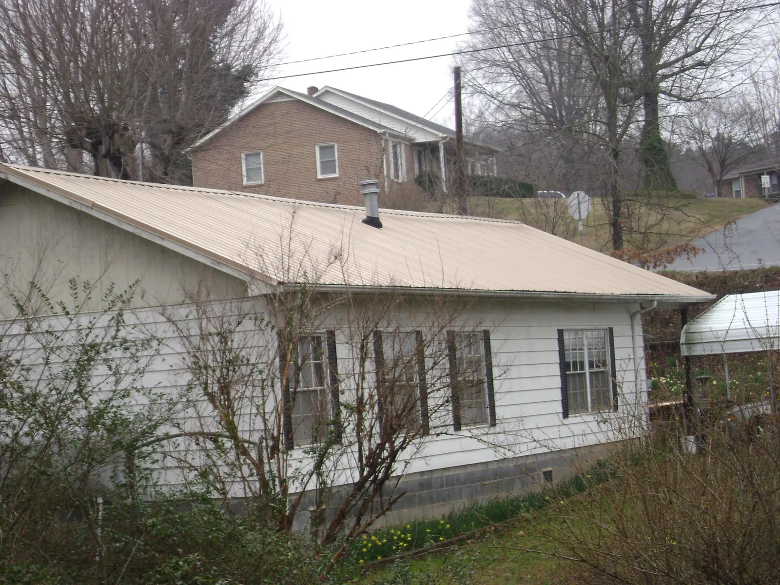 Tan metal roof on a white sided house set into a hillside — Commercial Roofing by Roofing Brothers in Point Lookout
